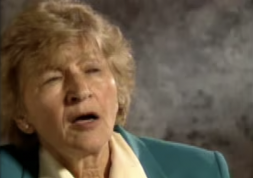 Old white women with short blond hair in front of a gray background.